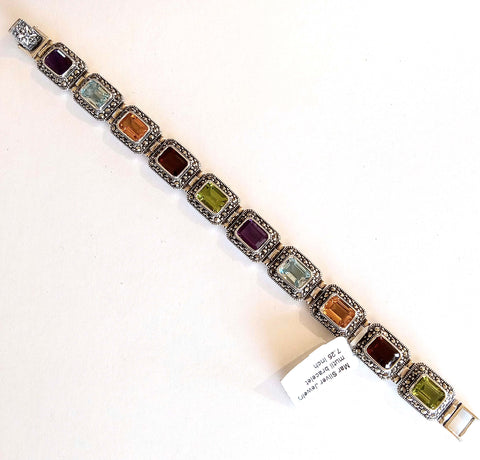 A multi-colored link bracelet with emerald cut amethyst, blue topaz, citrine, garnet, and peridot stones, surrounded by marcasite stones, on a white background.